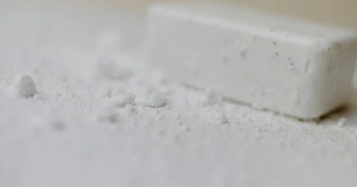 Pot de bicarbonate de soude ouvert avec une brosse et un chiffon microfibre sur plan de travail carrelé blanc