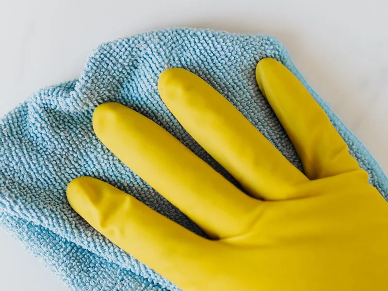 Gants de nettoyage jaunes tenant un chiffon bleu microfibre sur fond blanc