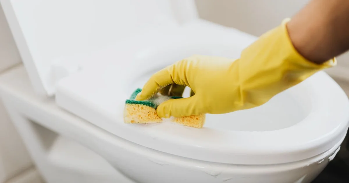 Main gantée de jaune nettoyant la cuvette des WC avec une éponge