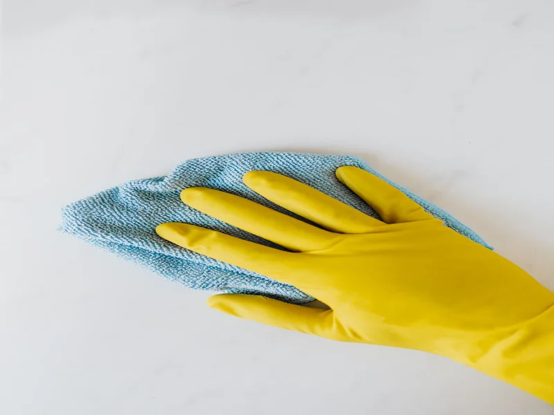 Main gantée jaune avec chiffon microfibre bleu essuyant une surface blanche