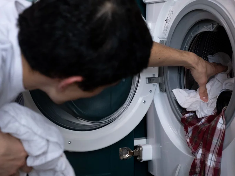 Personne retirant du linge d'une machine à laver à hublot ouverte