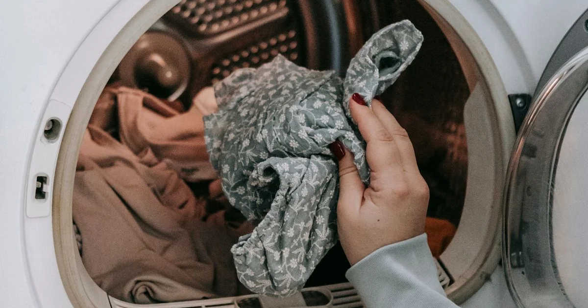 Main qui charge du linge fleuri dans un sèche-linge domestique prêt à être nettoyé